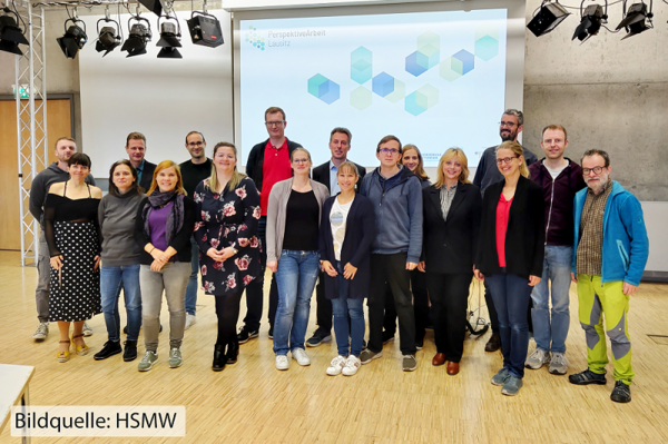 Knapp zwanzig Leute stehen für ein Gruppenfoto im Hörsaal vor der Präsentationsleinwand mit dem PAL-Logo